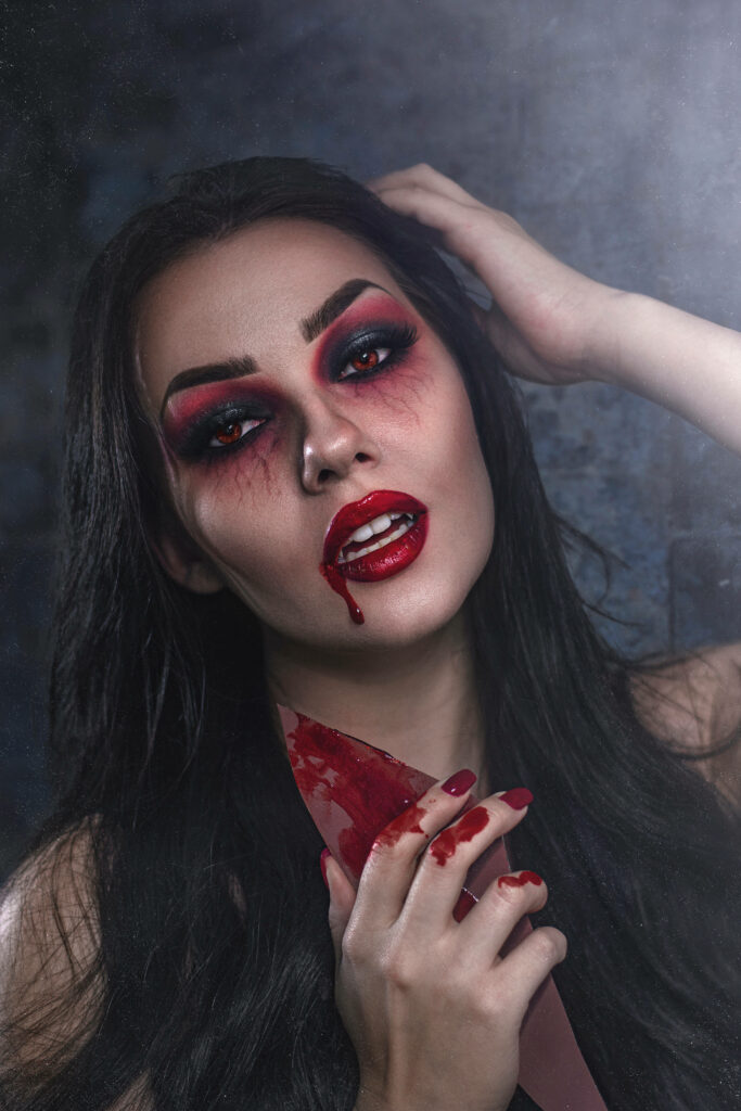Dark-haired vampire woman with red black makeup blood dripping knife intense wallpaper background