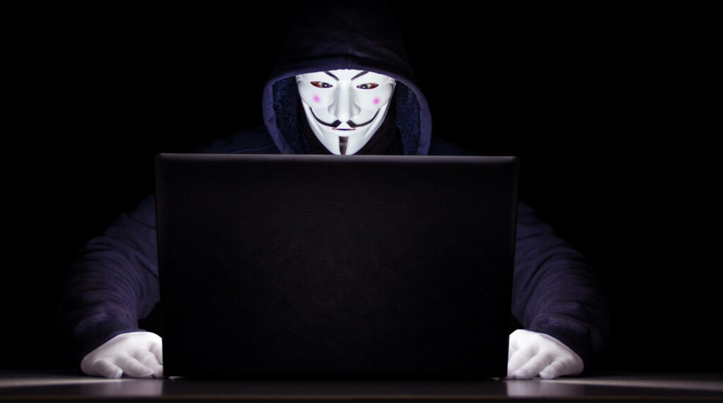 Intriguing Cyber Warrior: A Captivating Snapshot of a Man in a Blue Jacket and Hacker Mask Embracing the Digital Realm on a Dark Background Wallpaper