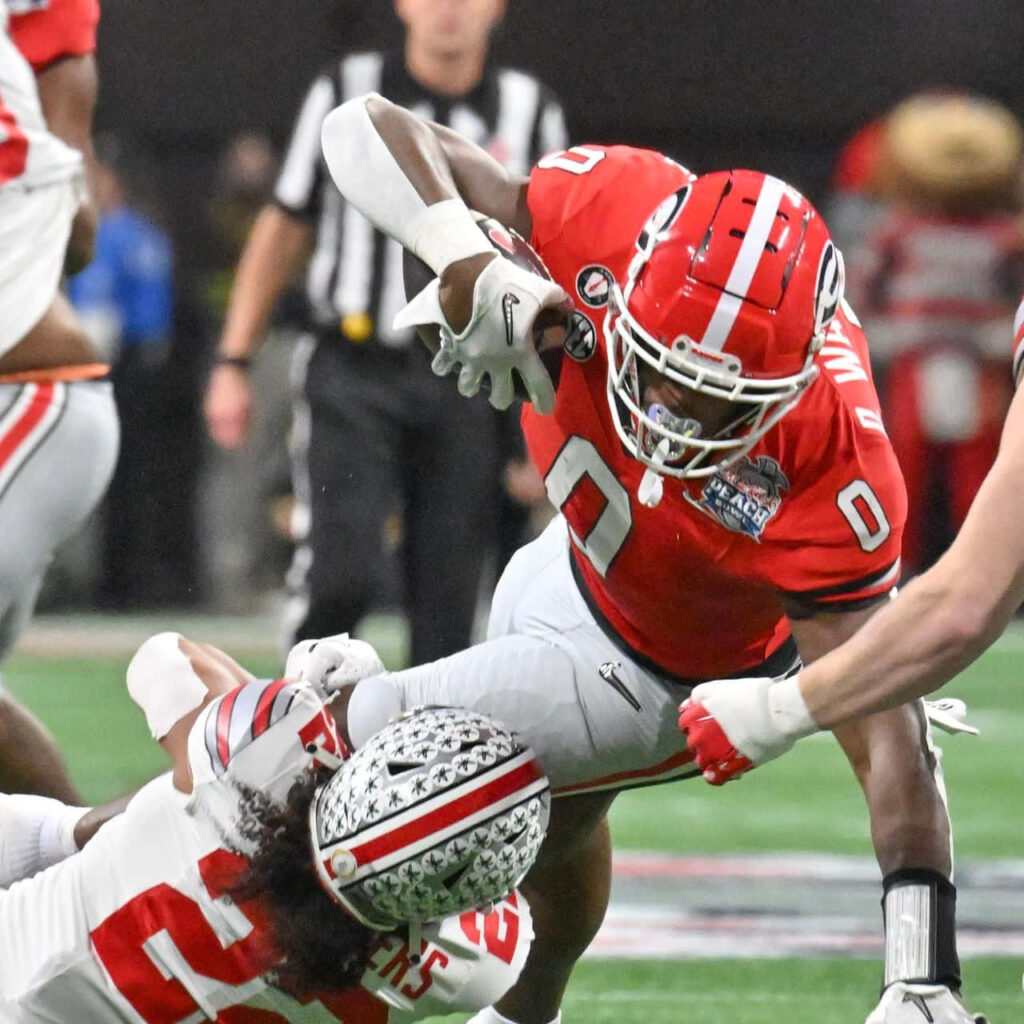 Darnell Washington in red white uniform powers through intense college football play action Wallpaper