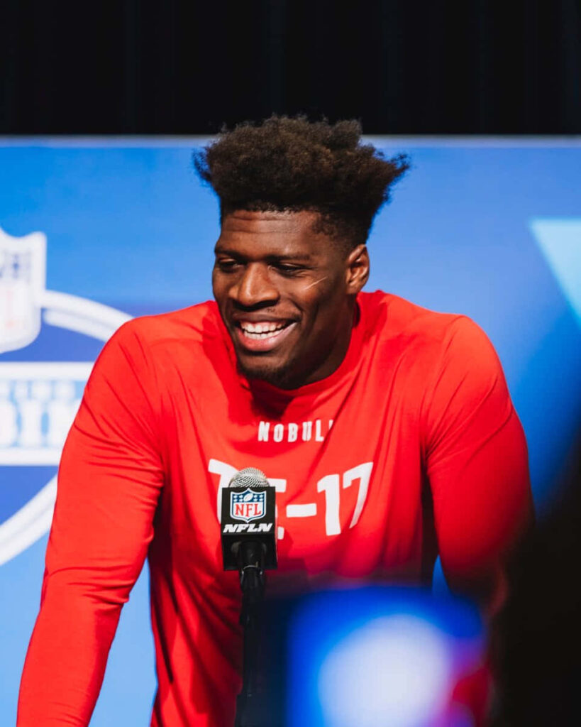 Darnell Washington smiling confidently at NFL event podium in bright red athletic shirt wallpaper