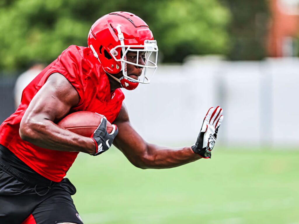 Darnell Washington sprinting with football in red uniform showcasing strength and focus on field Wallpaper