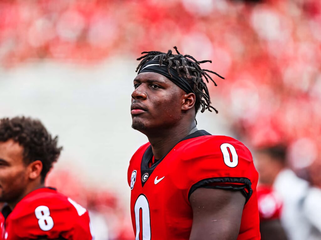 Darnell Washington in red jersey number 0 focused on football field with blurred red stadium background Wallpaper