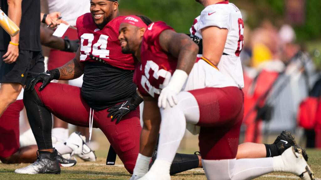 Daron Payne laughing in maroon and white football gear during sunny team training session Wallpaper