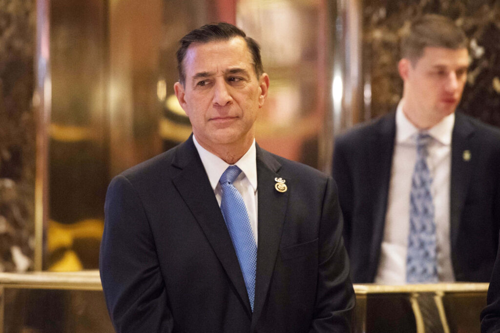 Darrell Issa in dark suit and blue tie looking sideways with warm golden blurred background Wallpaper