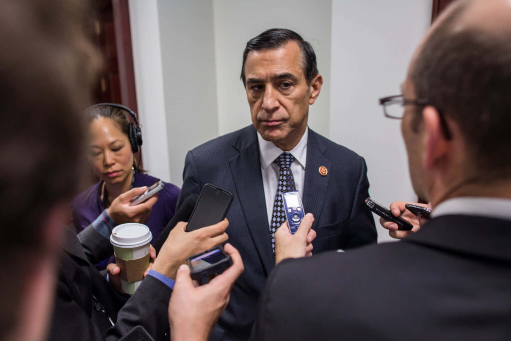 Darrell Issa in pinstripe suit speaks to media microphones and recorders in formal setting Wallpaper