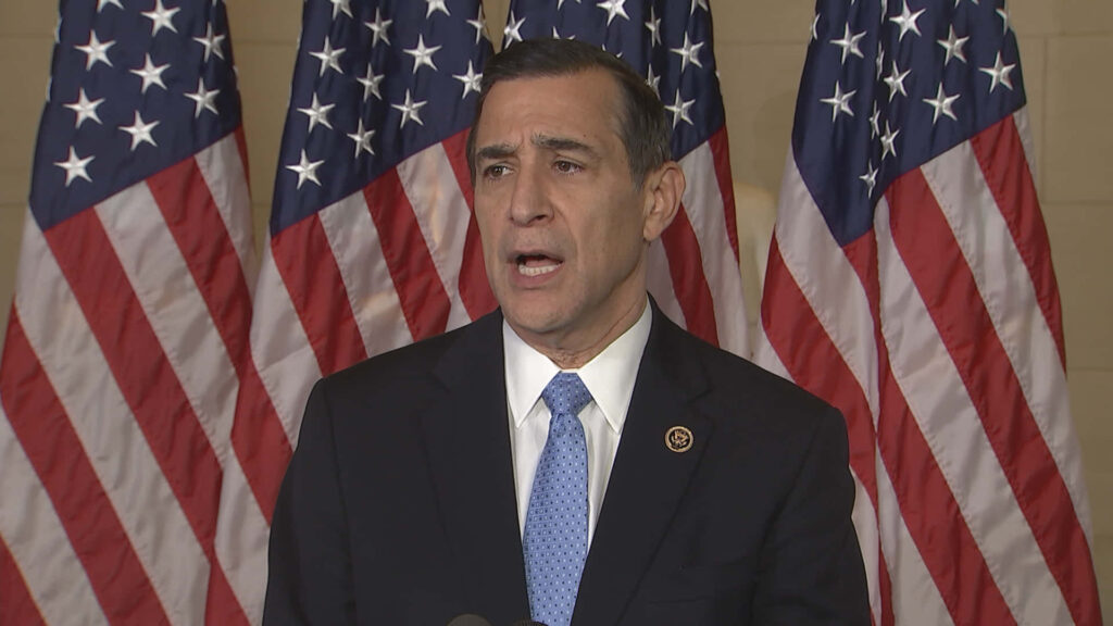 Darrell Issa in dark suit with blue tie stands before American flags showing leadership pride Wallpaper