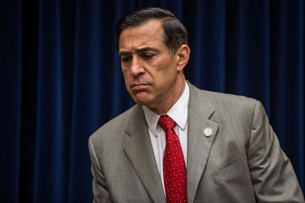 Darrell Issa in gray suit and red tie stands pensively against deep blue curtain background Wallpaper