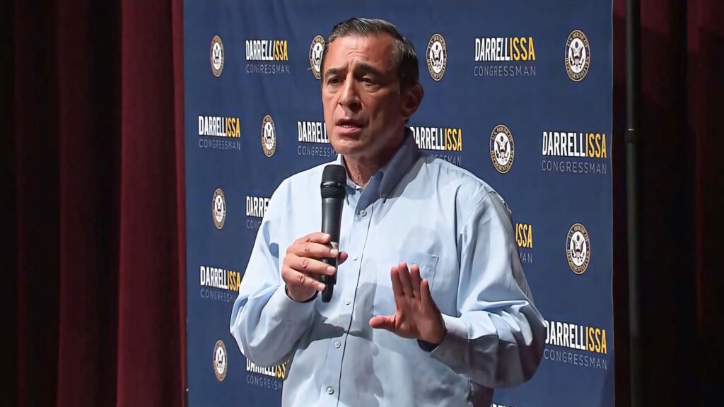 Darrell Issa speaking on stage with microphone and congressional seal backdrop in warm lighting Wallpaper