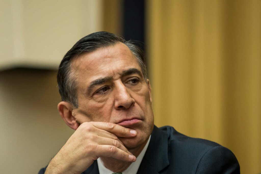 Darrell Issa thoughtful pose hand on chin warm tones professional setting contemplative expression Wallpaper