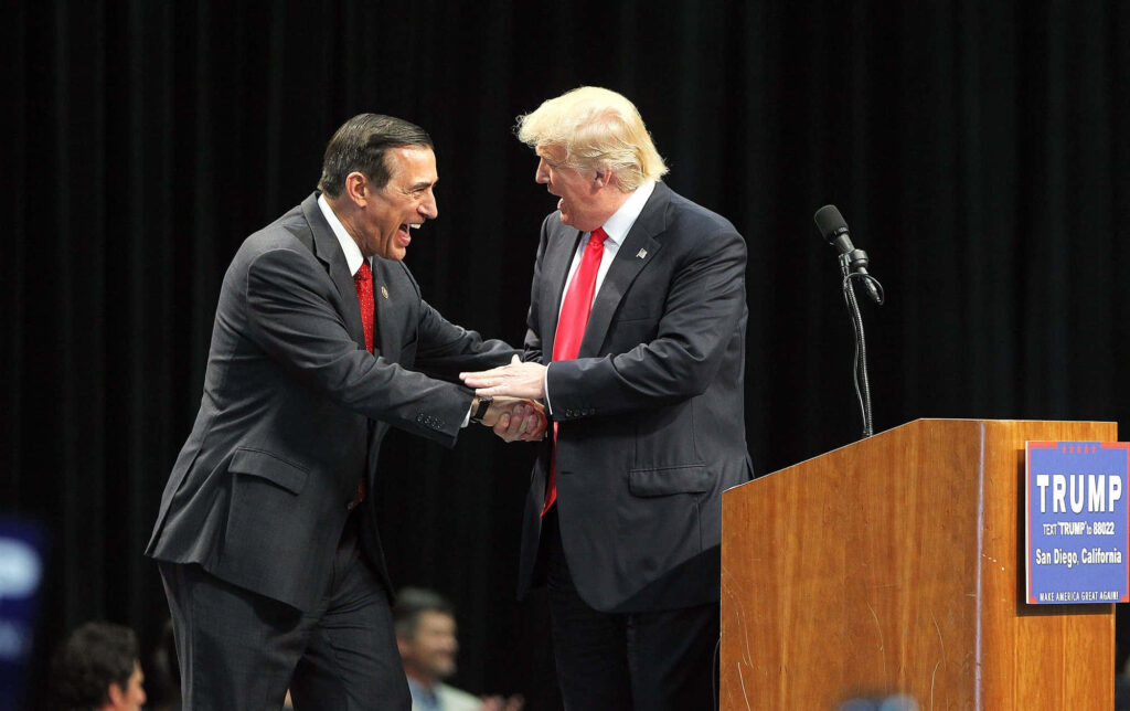 Darrell Issa and Donald Trump shaking hands on stage at political event with campaign podium Wallpaper