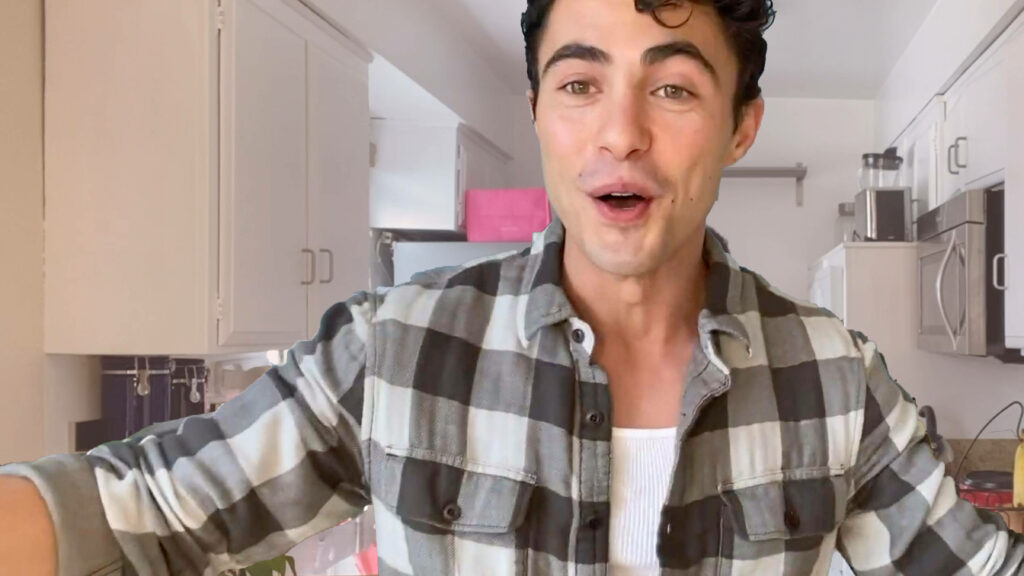 Darren Barnet in checkered shirt posing in bright modern kitchen with natural daylight wallpaper background