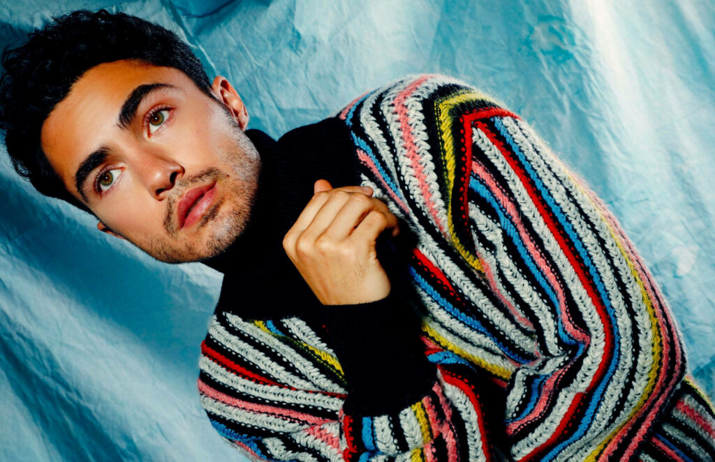 Darren Barnet in colorful striped knit sweater posing against blue textured background fashion portrait Wallpaper