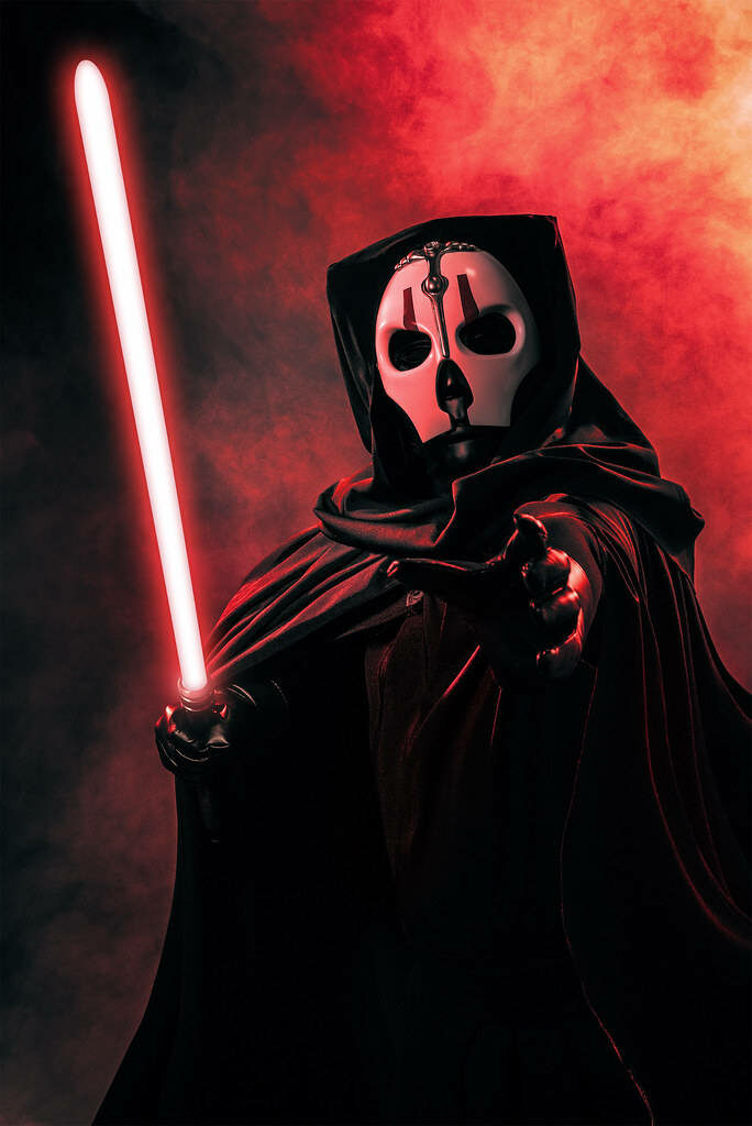 Darth Nihilus in dark hood with white mask wields glowing red lightsaber in smoky Sith scene Wallpaper