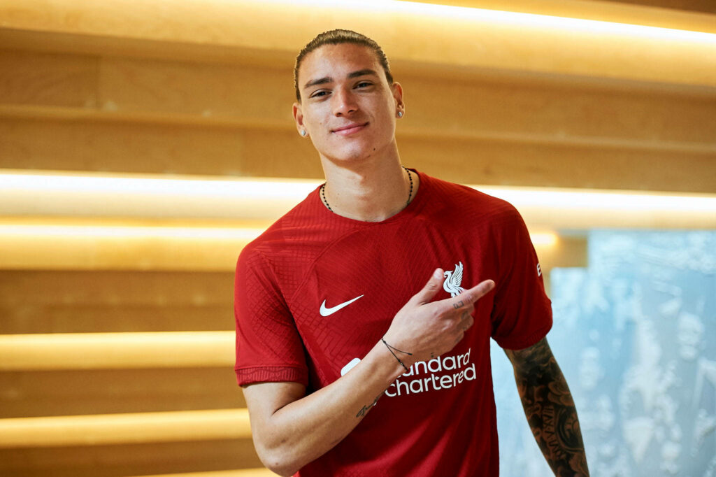 Darwin Núñez in Liverpool jersey making dynamic Nike gesture with warm wooden background lighting Wallpaper