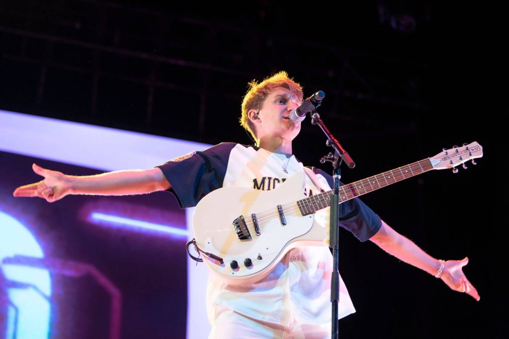 Dave Bayley of Glass Animals sings and plays white Danelectro guitar on vibrant blue stage Wallpaper