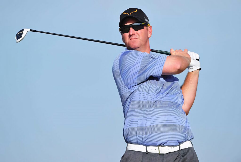 David Duval in blue-striped shirt confidently posing with golf club against clear sky background Wallpaper
