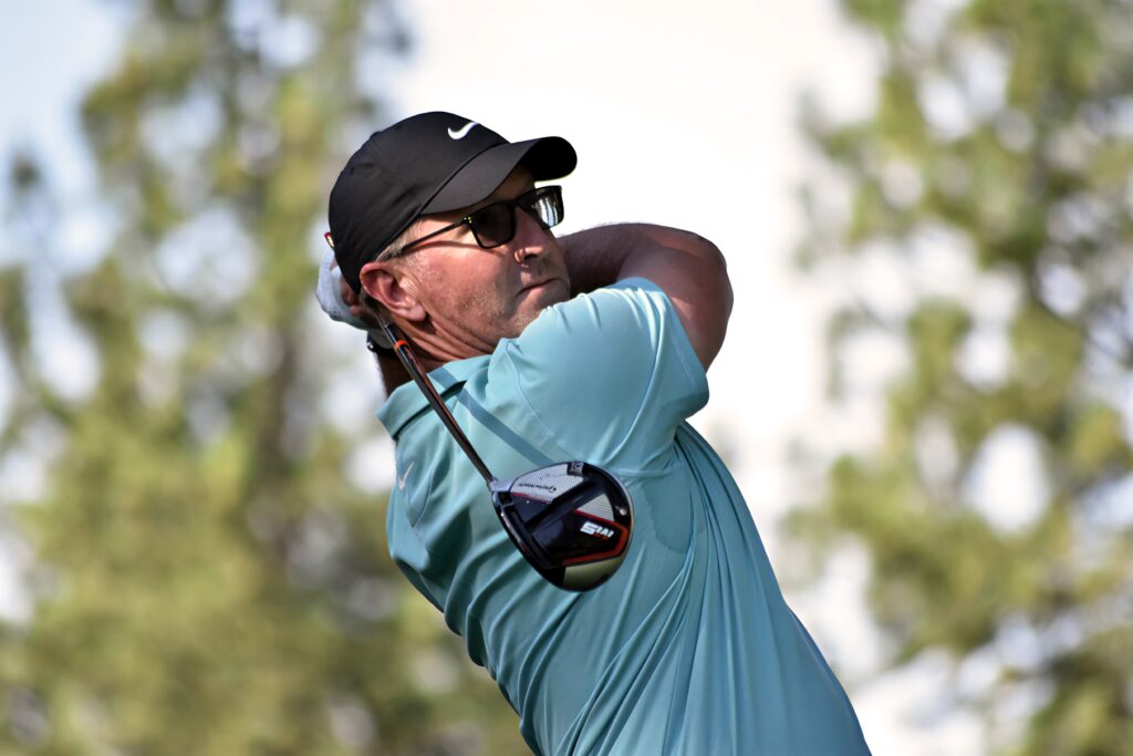 David Duval mid golf swing wearing blue polo black cap sunglasses with blurred outdoor golf course background Wallpaper