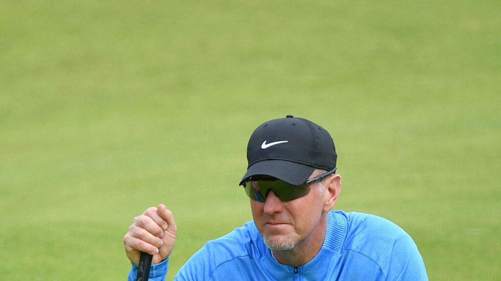 David Duval focused on golf course wearing blue sweater black cap sunglasses lush green background Wallpaper
