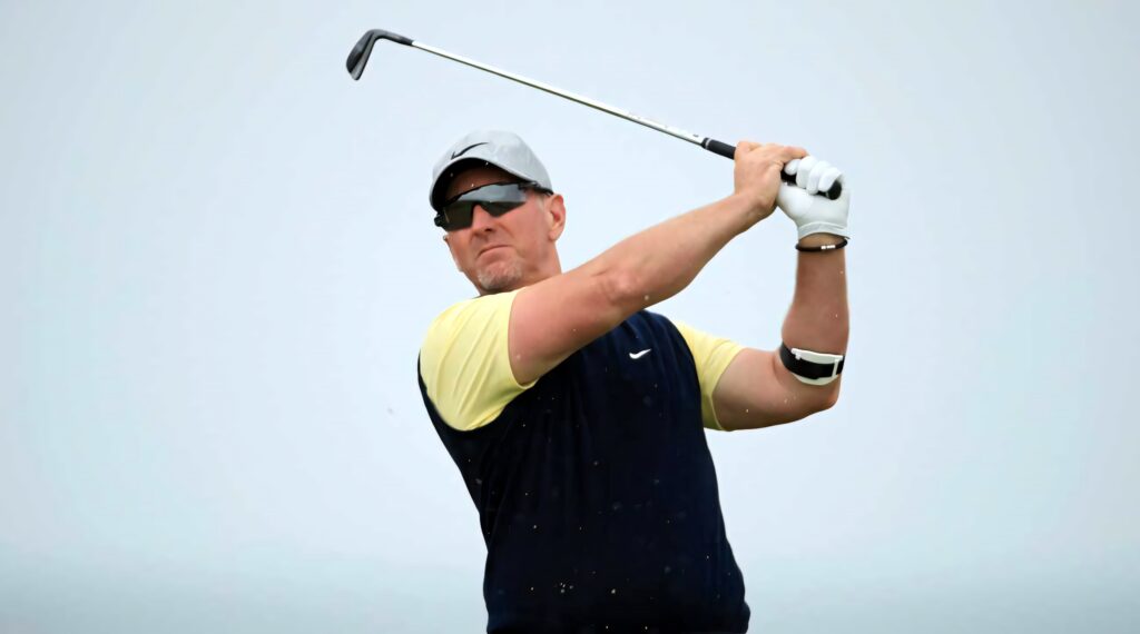 David Duval mid golf swing wearing cap sunglasses athletic stance sharp focus muted sky wallpaper background