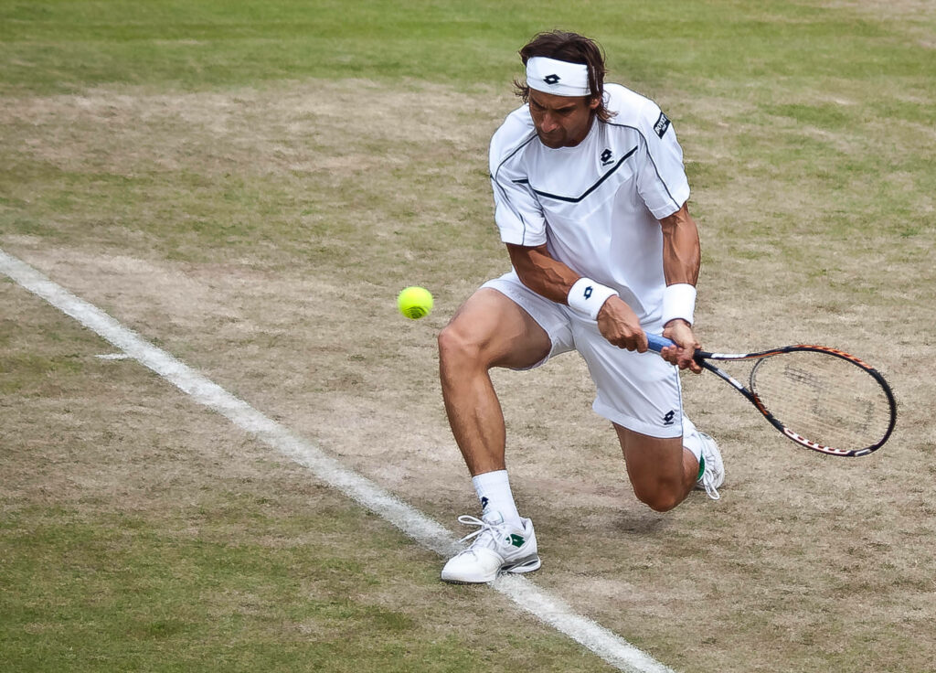 David Ferrer kneeling on grass tennis court returning low shot showcasing athleticism and focus Wallpaper