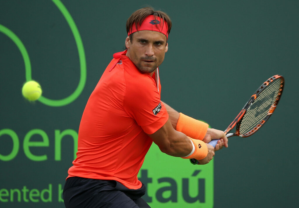 David Ferrer in vivid orange shirt and headband focused during intense tennis match on green court Wallpaper