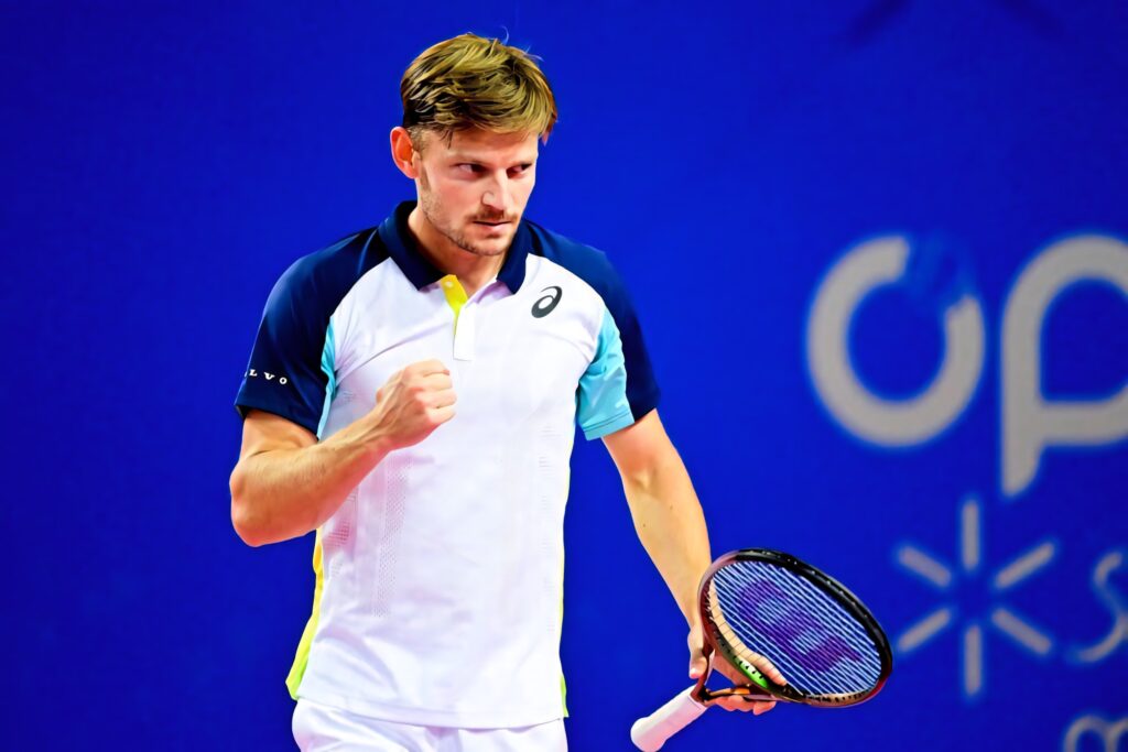 David Goffin celebrating intense tennis backhand shot in white and navy sportswear on blue background Wallpaper