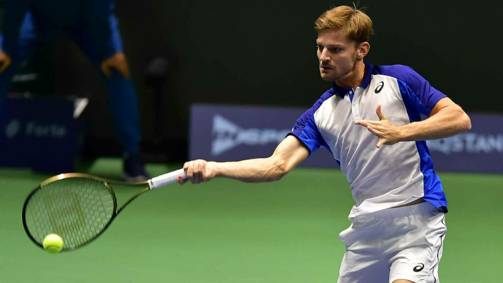 David Goffin hitting forehand on indoor tennis court wearing blue white sportswear in action pose Wallpaper
