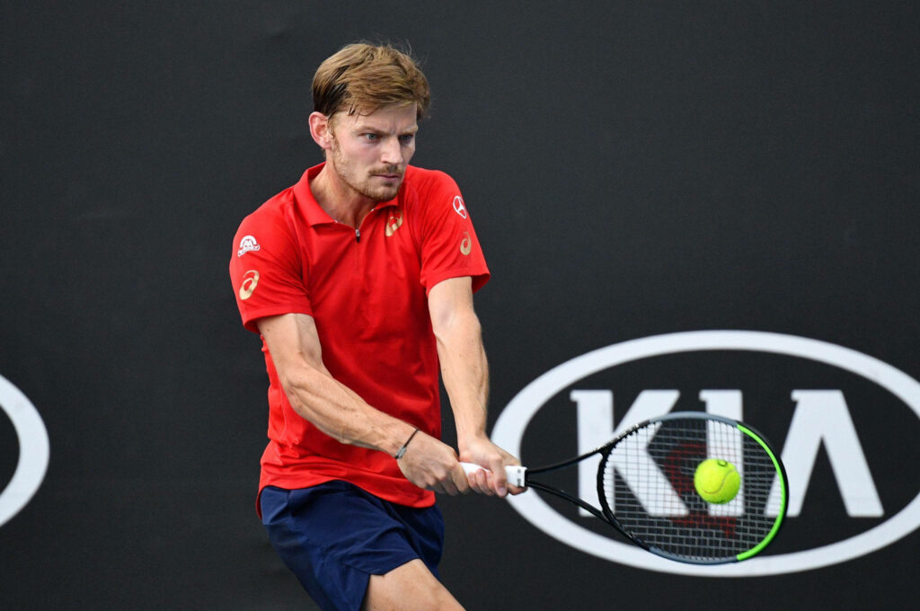 David Goffin in red shirt focused preparing to receive tennis ball mid action on court wallpaper