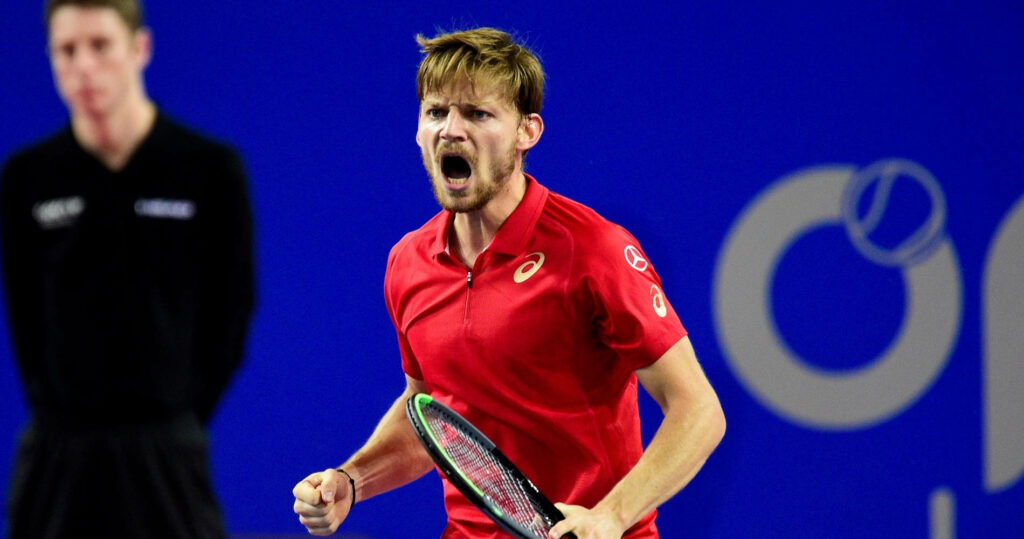 David Goffin shouting triumphantly in red shirt holding racket with vibrant blue tennis court background Wallpaper