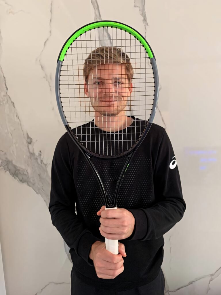 David Goffin behind tennis racket strings focused expression black outfit marble background Wallpaper