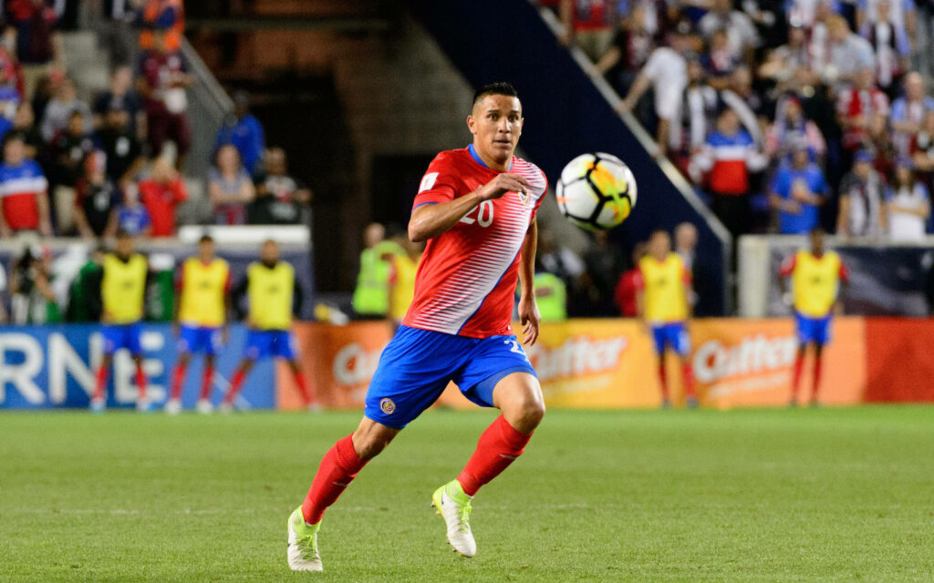 David Guzman sprinting in red blue Costa Rica football kit at vibrant stadium full of fans Wallpaper