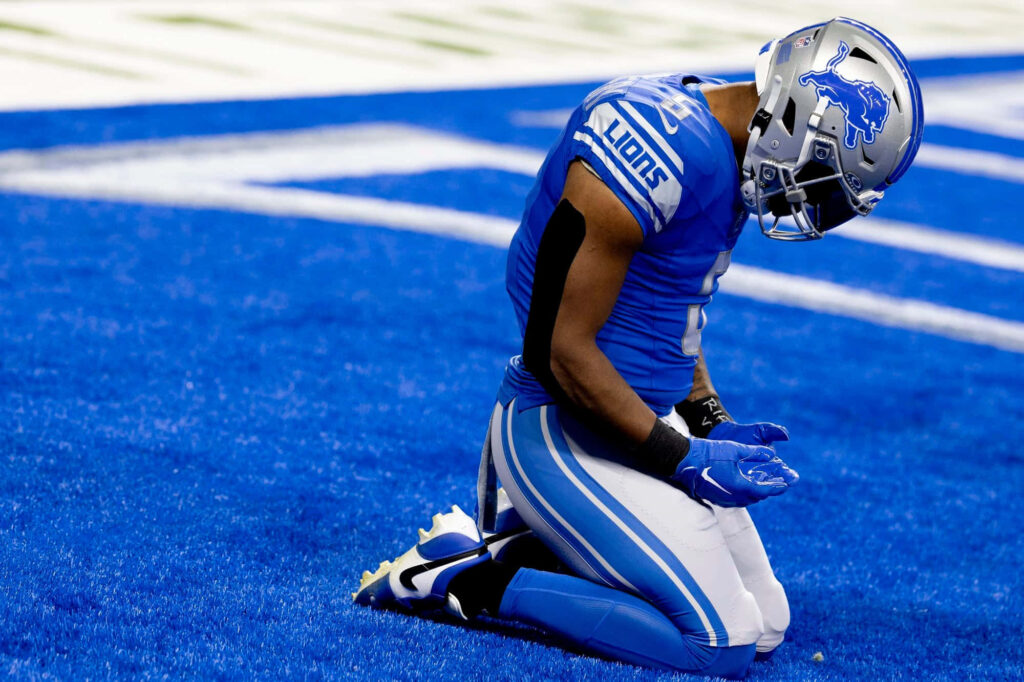Detroit Lions running back David Montgomery kneeling on blue field in full uniform showing focus Wallpaper