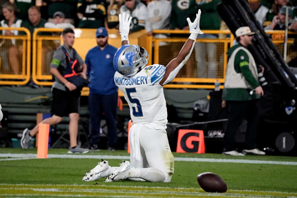 David Montgomery Detroit Lions touchdown celebration kneeling with arms raised on vibrant field Wallpaper