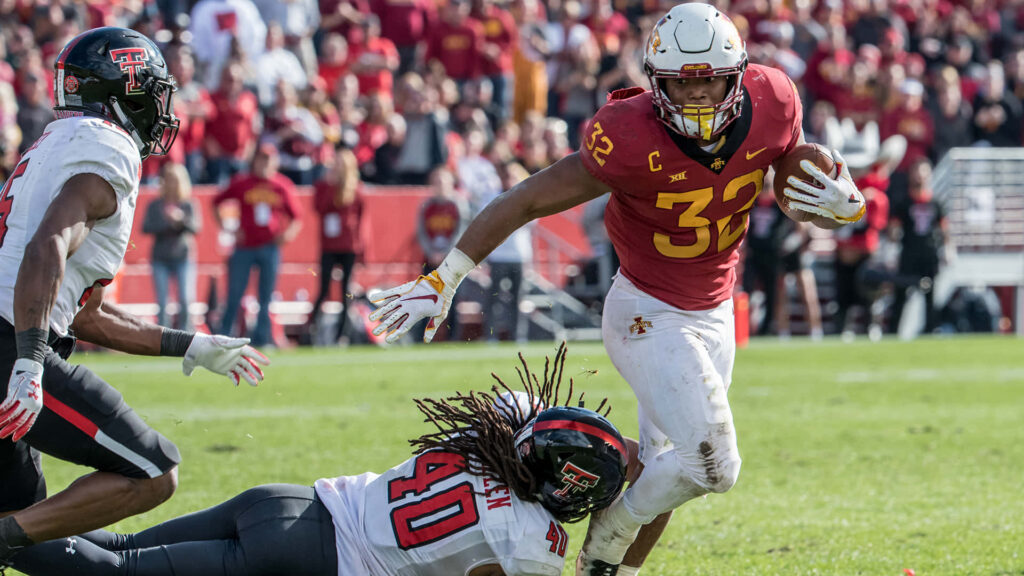 David Montgomery in Iowa State football uniform powerfully running past Texas Tech defenders on sunlit field Wallpaper