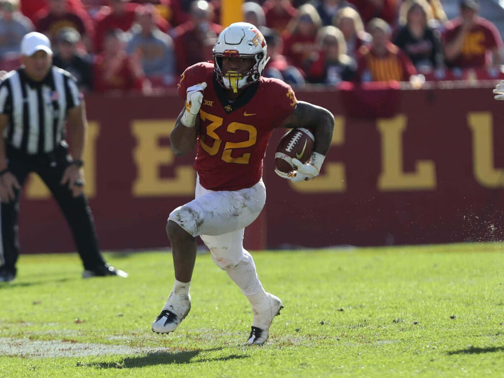 David Montgomery running back sprinting in red gold uniform on sunlit football field vibrant stadium Wallpaper