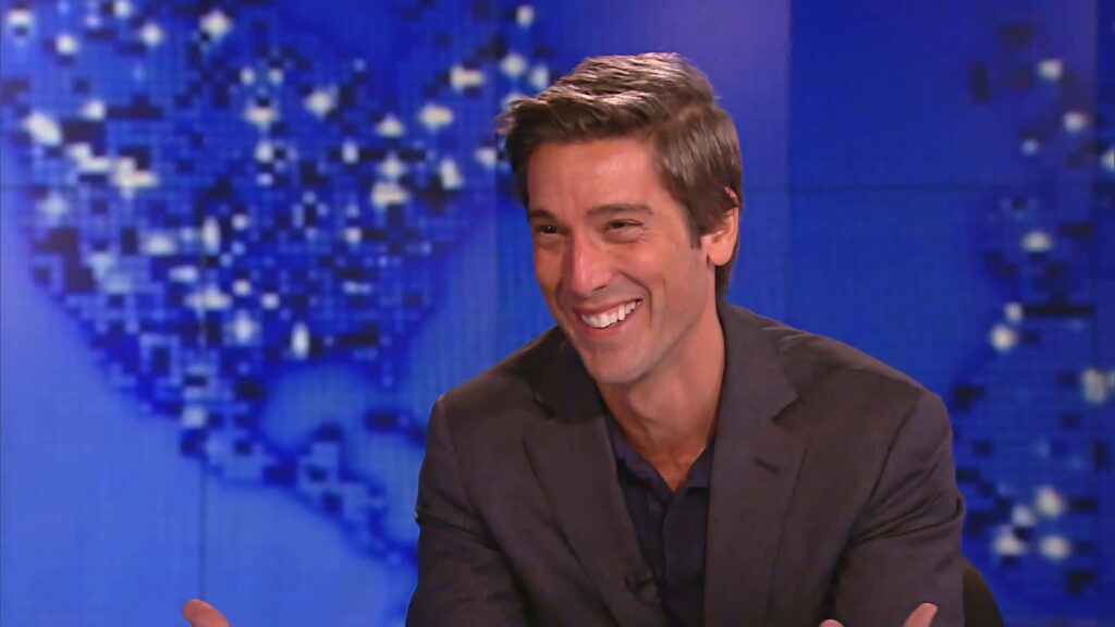 David Muir smiling confidently in sharp suit against blurred blue digital world map background Wallpaper