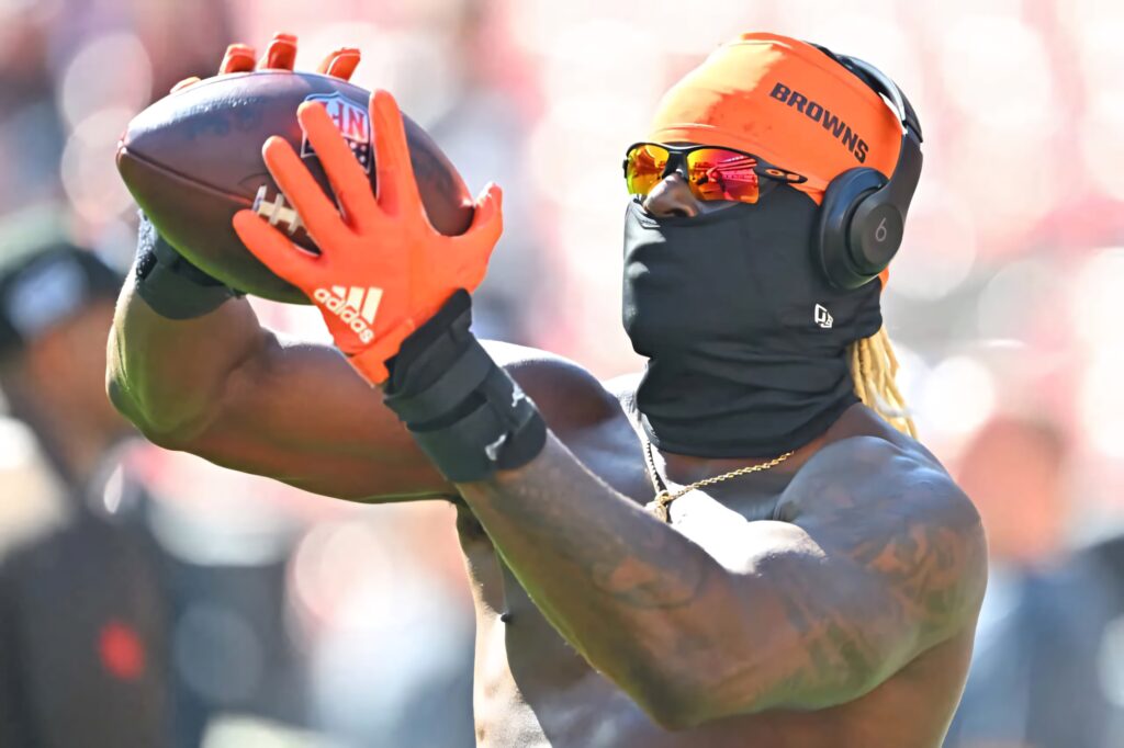 David Njoku focused catching football wearing orange gloves sunglasses headphones Browns colors Wallpaper