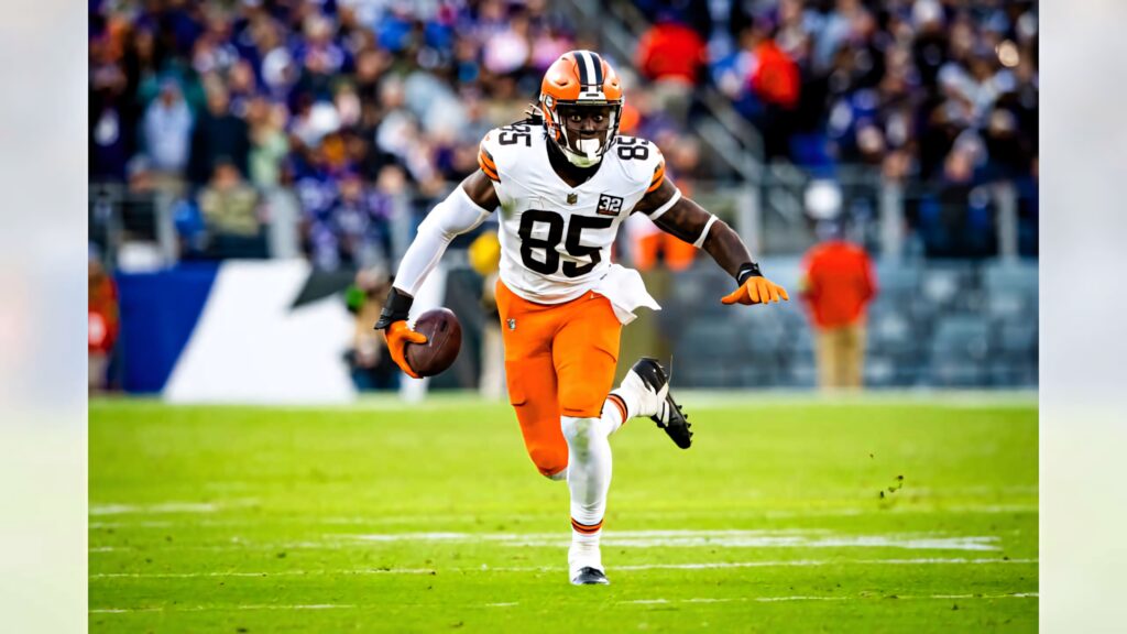 David Njoku Cleveland Browns mid-action in orange brown uniform with blurred stadium crowd background Wallpaper