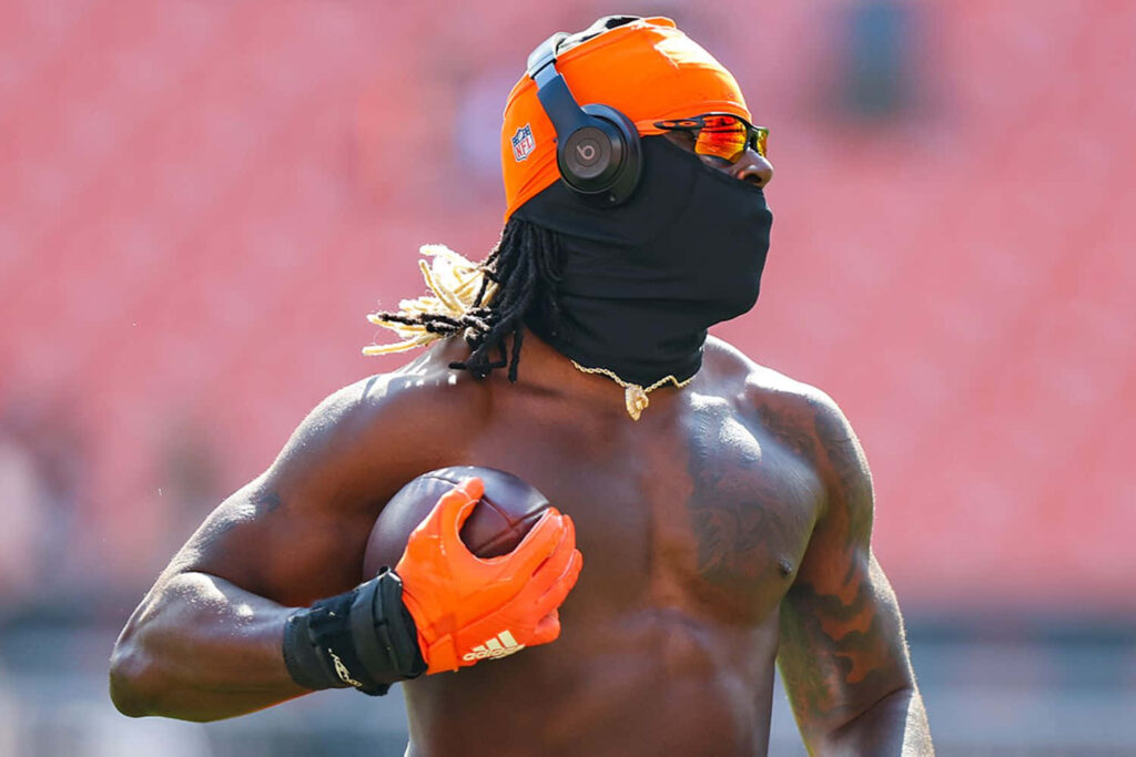 David Njoku football warmup bright orange gear headphones sunglasses holding ball vivid stadium background Wallpaper