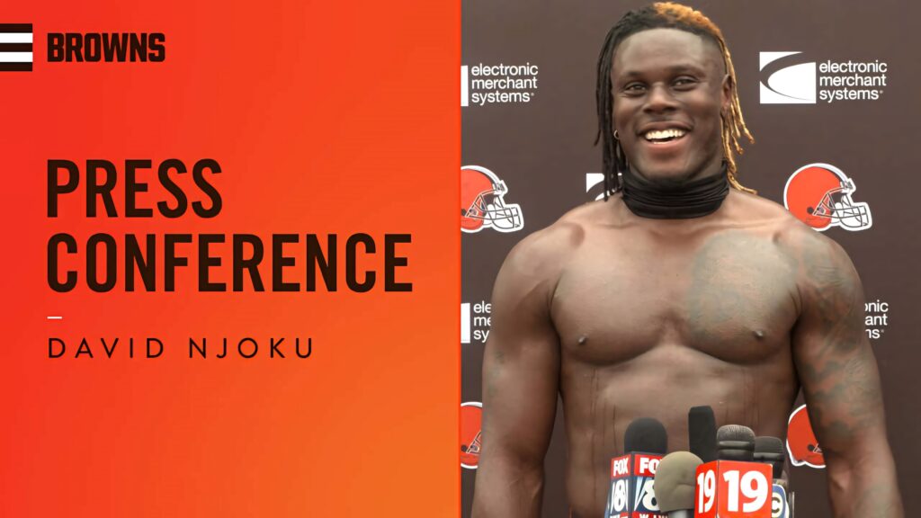 David Njoku shirtless smiling at Cleveland Browns press conference with team logos and microphones Wallpaper