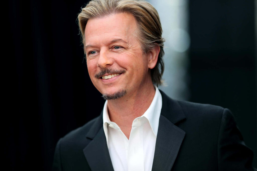 David Spade in classic black suit white shirt smiling against soft blurred dark background wallpaper
