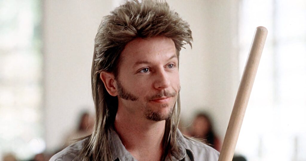 David Spade classic mullet hairstyle holding wooden stick soft lighting blurred background wallpaper