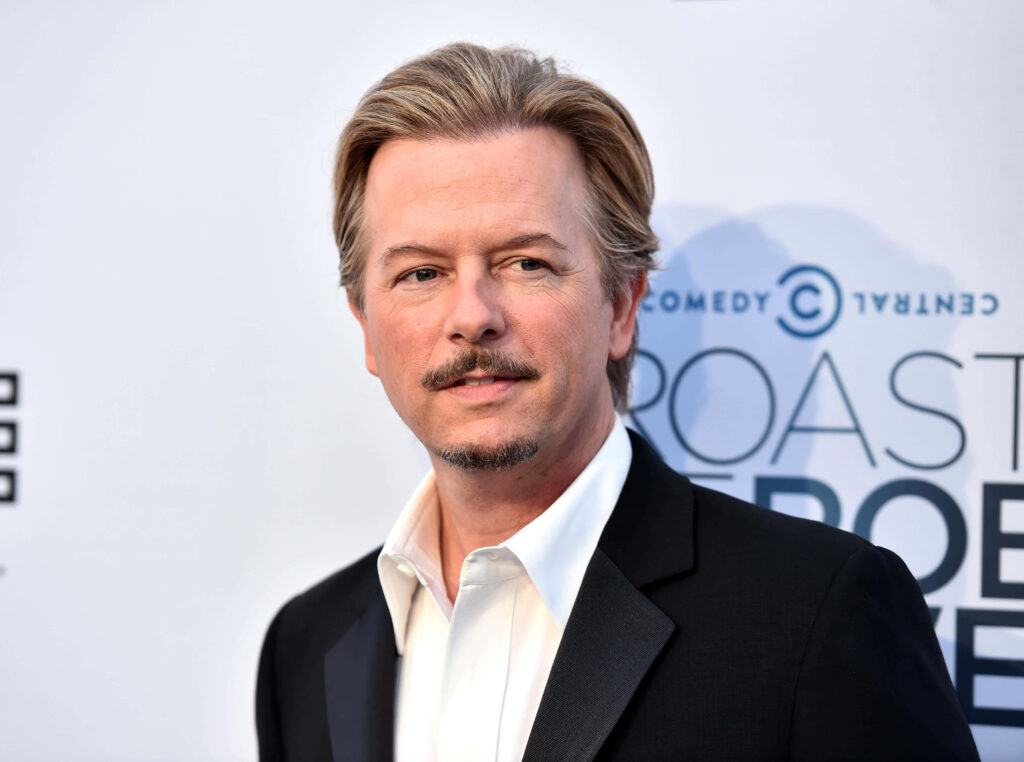 David Spade in black suit at formal event with Comedy Central logo and soft lighting background Wallpaper