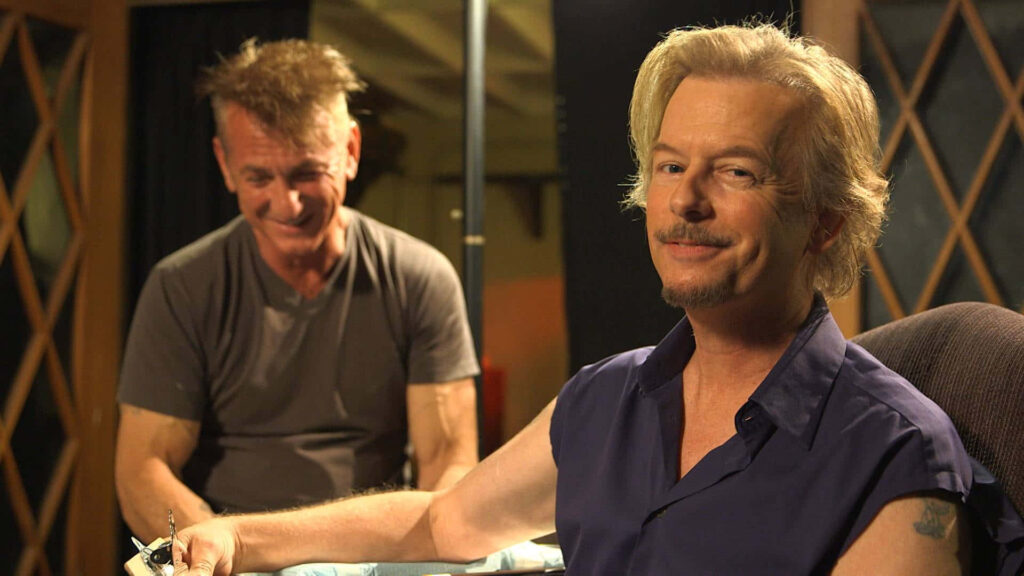 David Spade with sly smile in casual setting warm lighting candid interaction wallpaper background