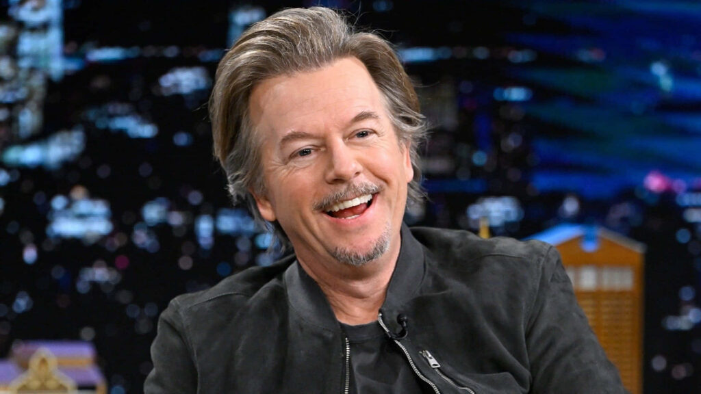 David Spade smiling warmly with blurred cityscape night background comedy wallpaper