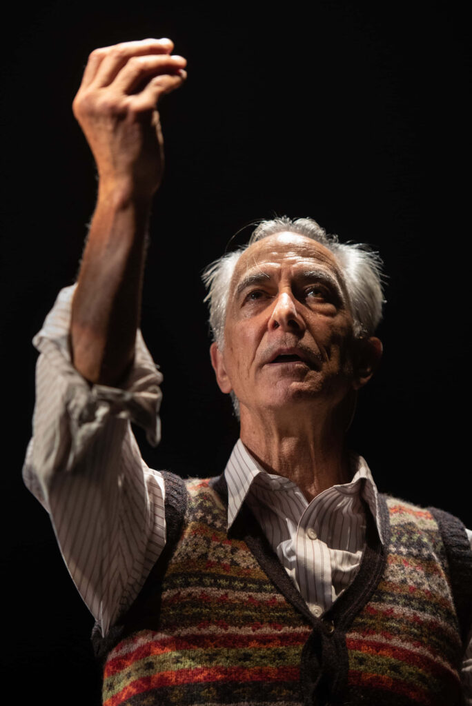 David Strathairn in dramatic light wearing sweater vest thoughtful pose dark cinematic background Wallpaper