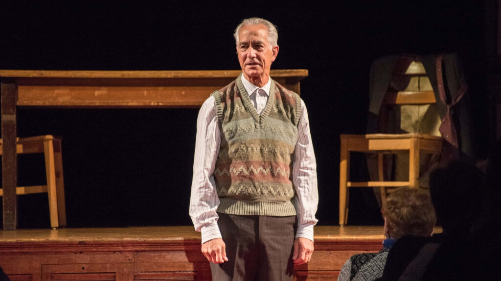 David Strathairn on wooden stage wearing patterned sweater vest in intimate theatrical setting Wallpaper