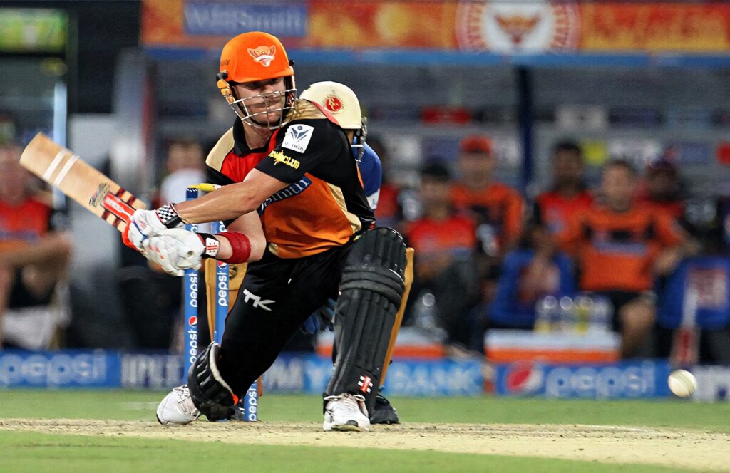 David Warner playing aggressive shot for Sunrisers Hyderabad in IPL match vibrant stadium Wallpaper