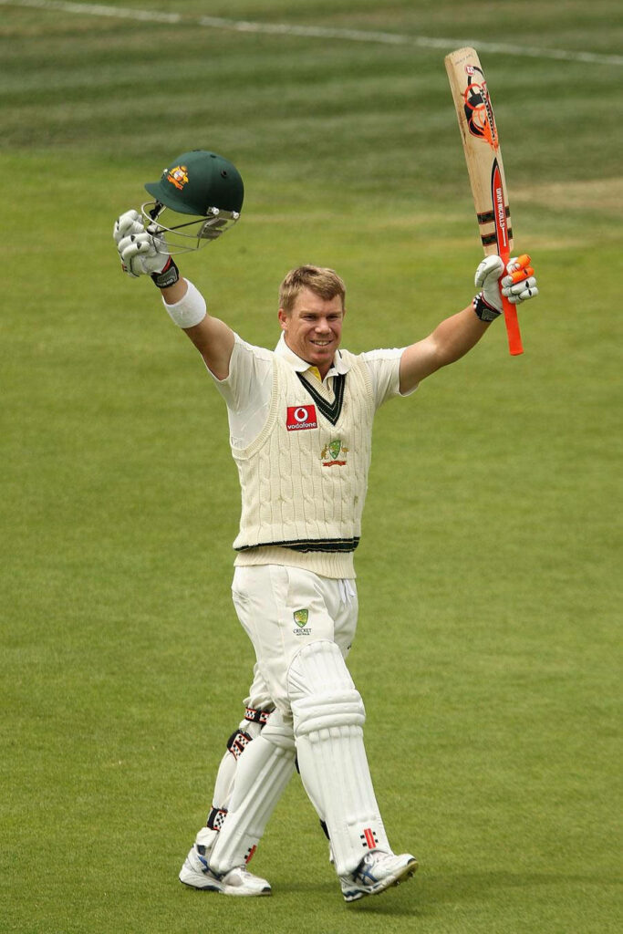 David Warner celebrates victory on cricket field holding helmet and bat in Australian Test uniform Wallpaper