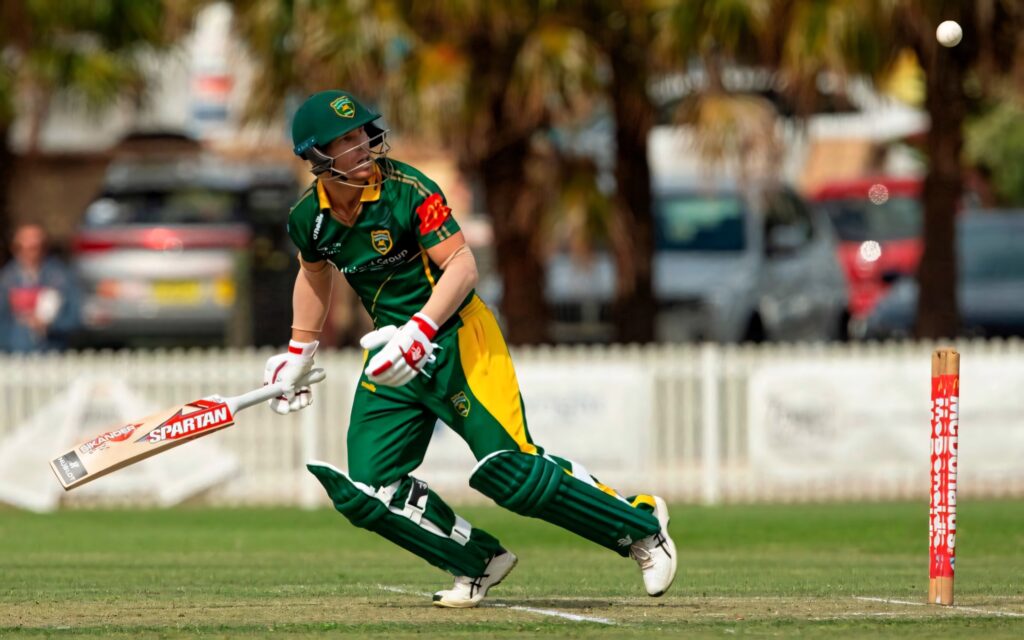 David Warner running on cricket field in green and yellow uniform showing focus and athleticism Wallpaper